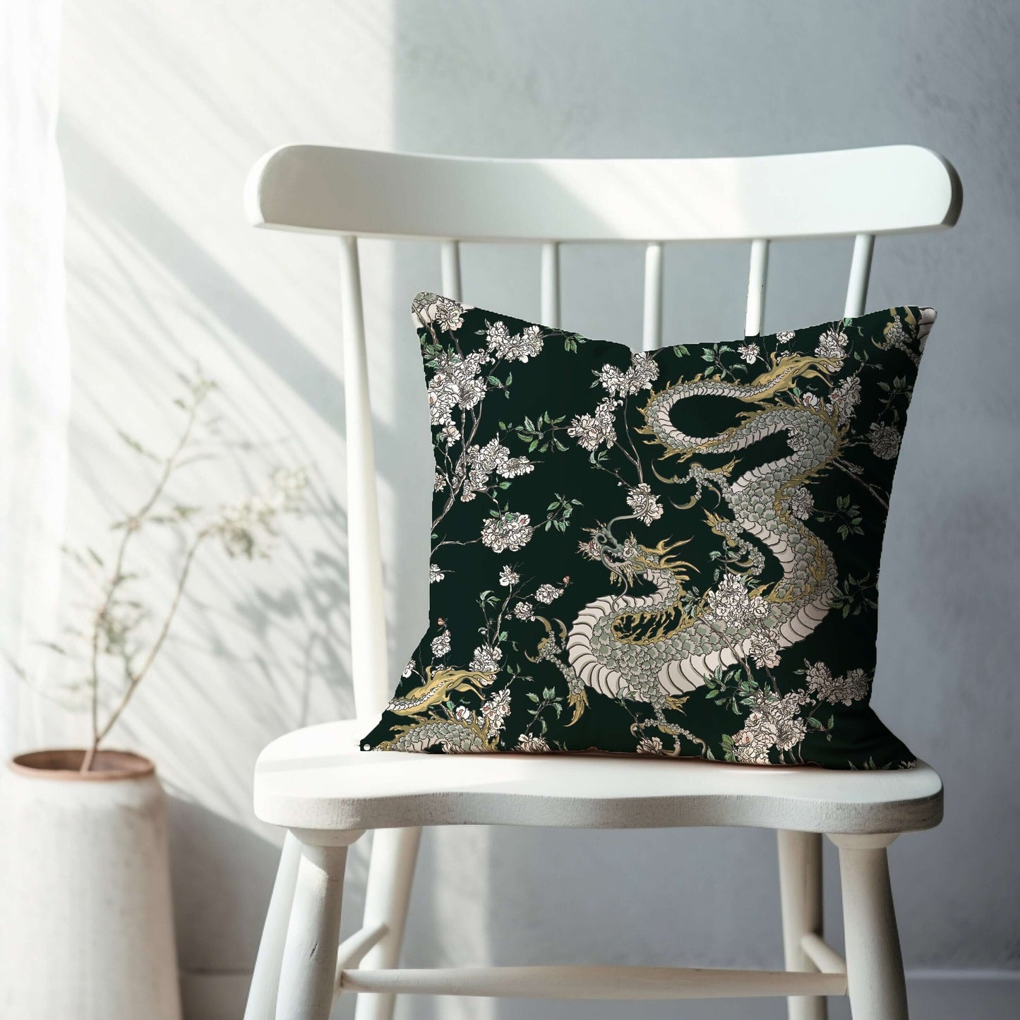 Dark green chinoiserie pillow with dragon and floral design. Oriental decorative pillow on white chair.