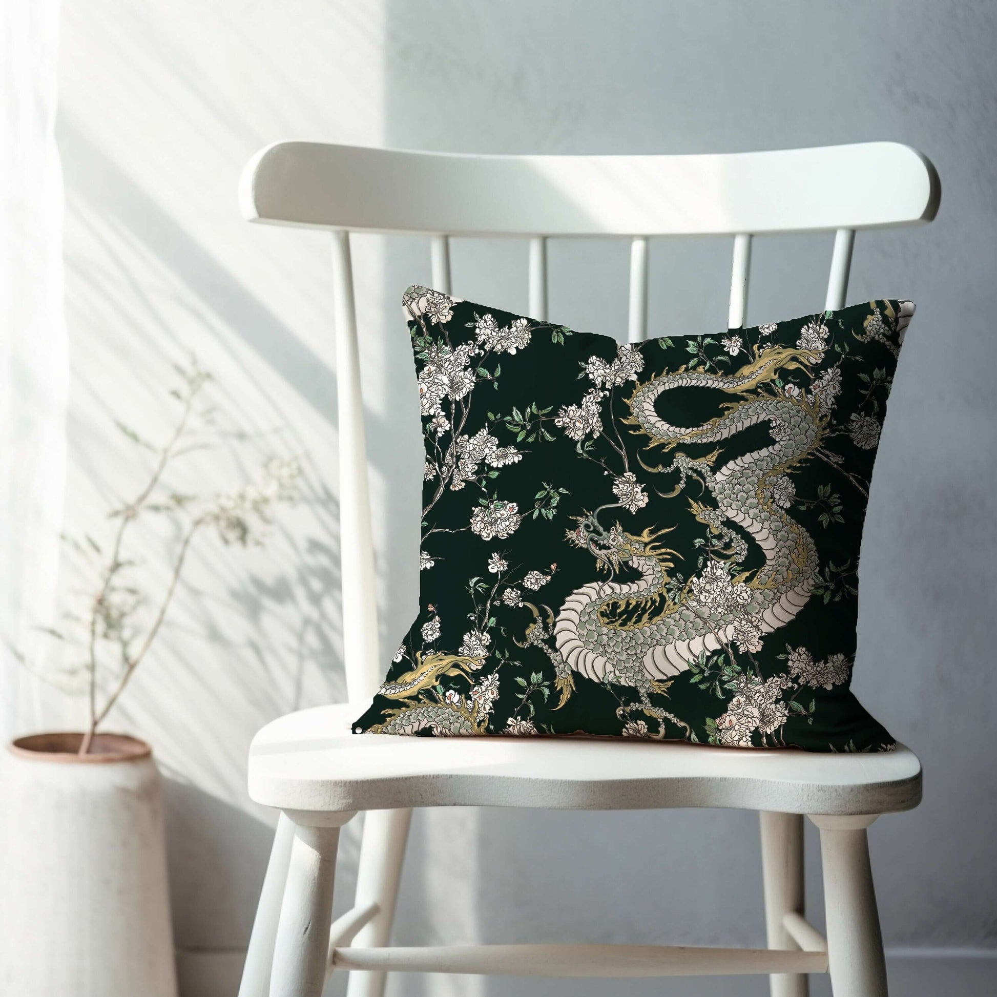 Dark green chinoiserie pillow with dragon and floral design. Oriental decorative pillow on white chair.