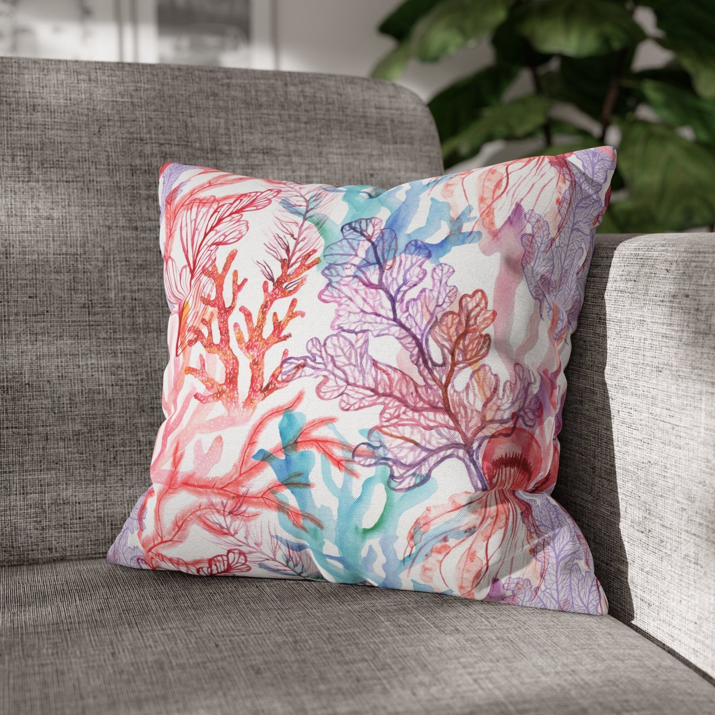 Coral reef pillow on grey sofa with plant. Ocean-themed decorative pillow with coral and jellyfish design.