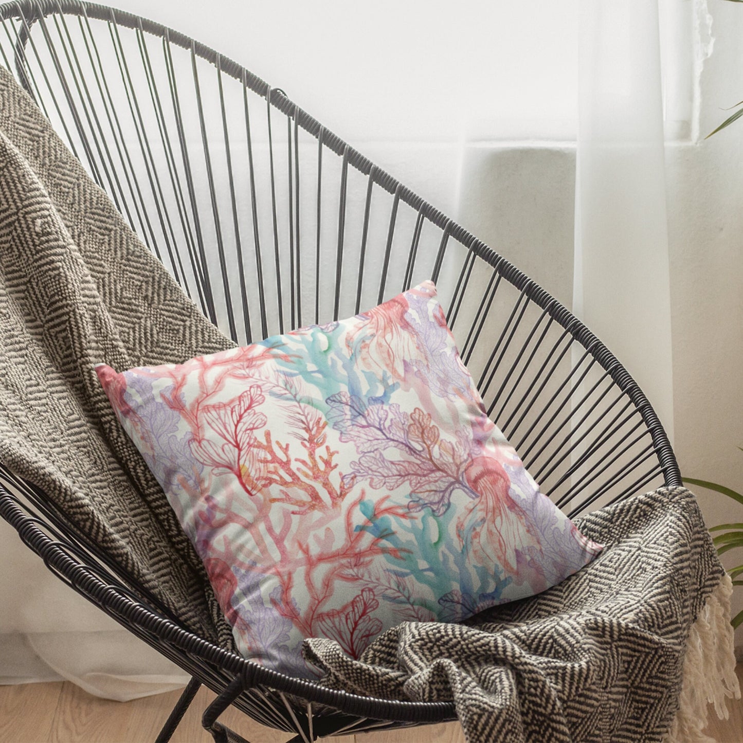 Coral reef pillow on black chair with window view. Ocean-themed decorative pillow with coral and jellyfish design.
