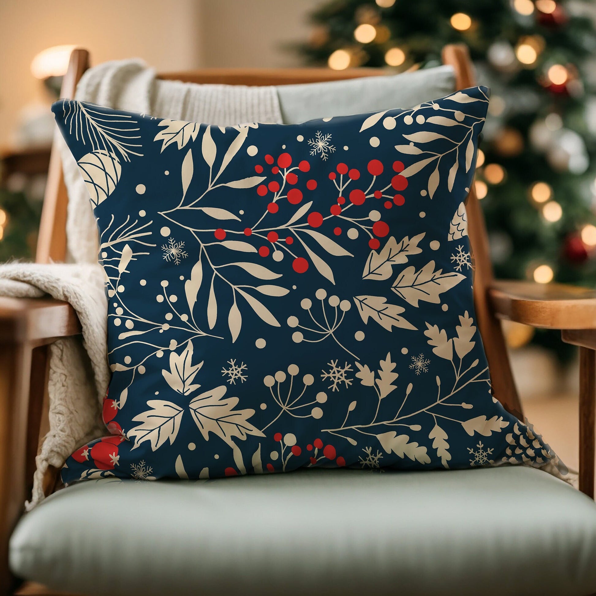 Navy winter botanical pillow with cream leaves, pinecones, snowflakes, and red berries on chair by Christmas tree