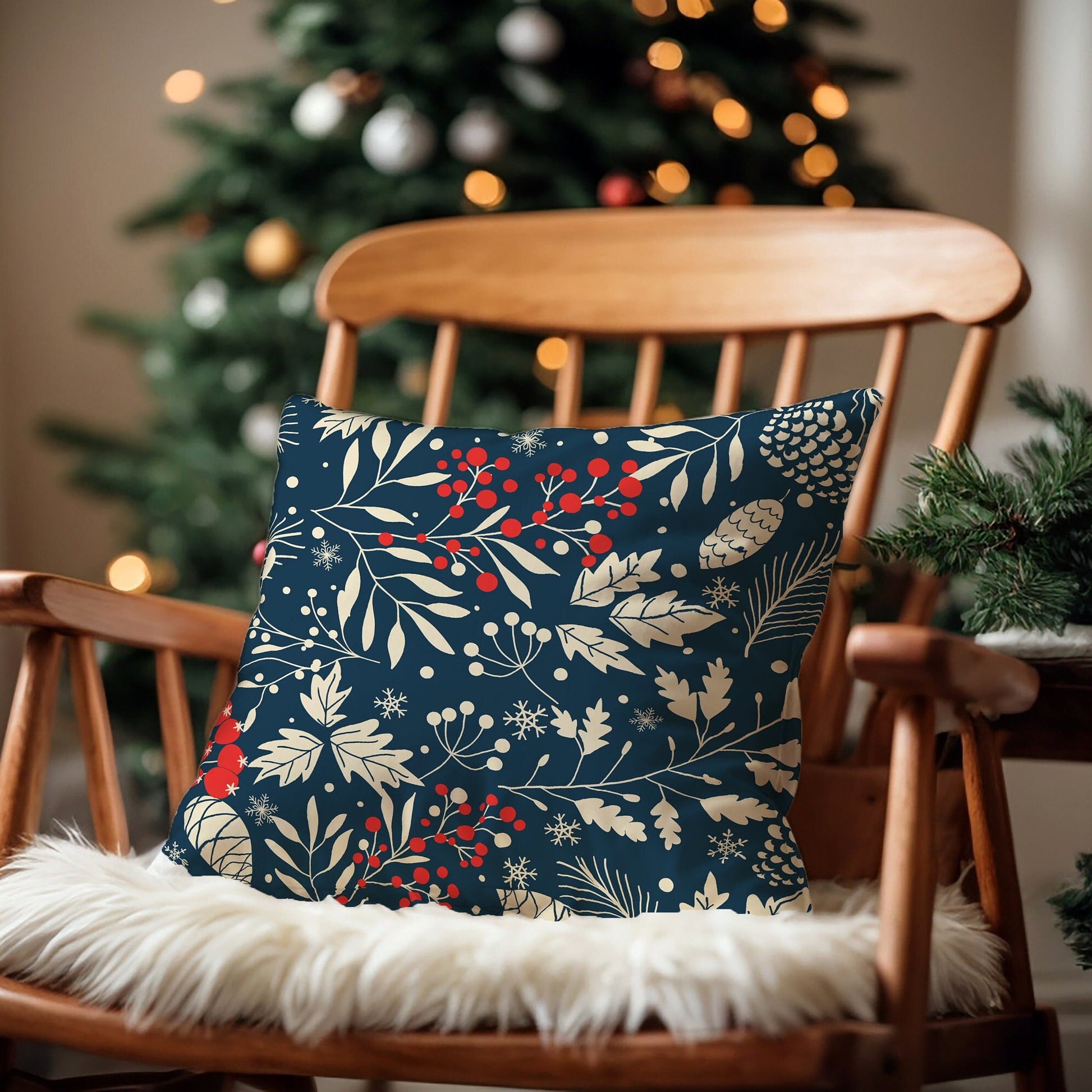 Navy winter botanical pillow with cream leaves, pinecones, and red berries on wooden chair by Christmas tree