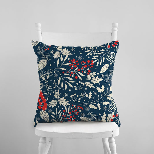 Navy botanical pillow with cream leaves, pinecones, snowflakes and red berries on a white chair