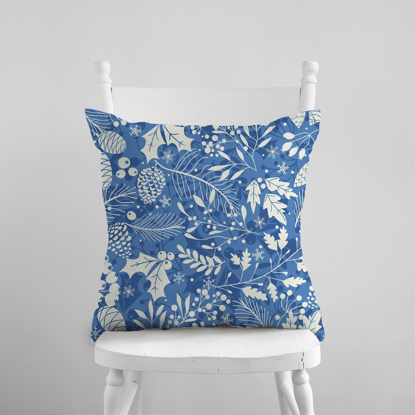 Light blue pillow with cream pinecones, leaves, and snowflakes on white chair